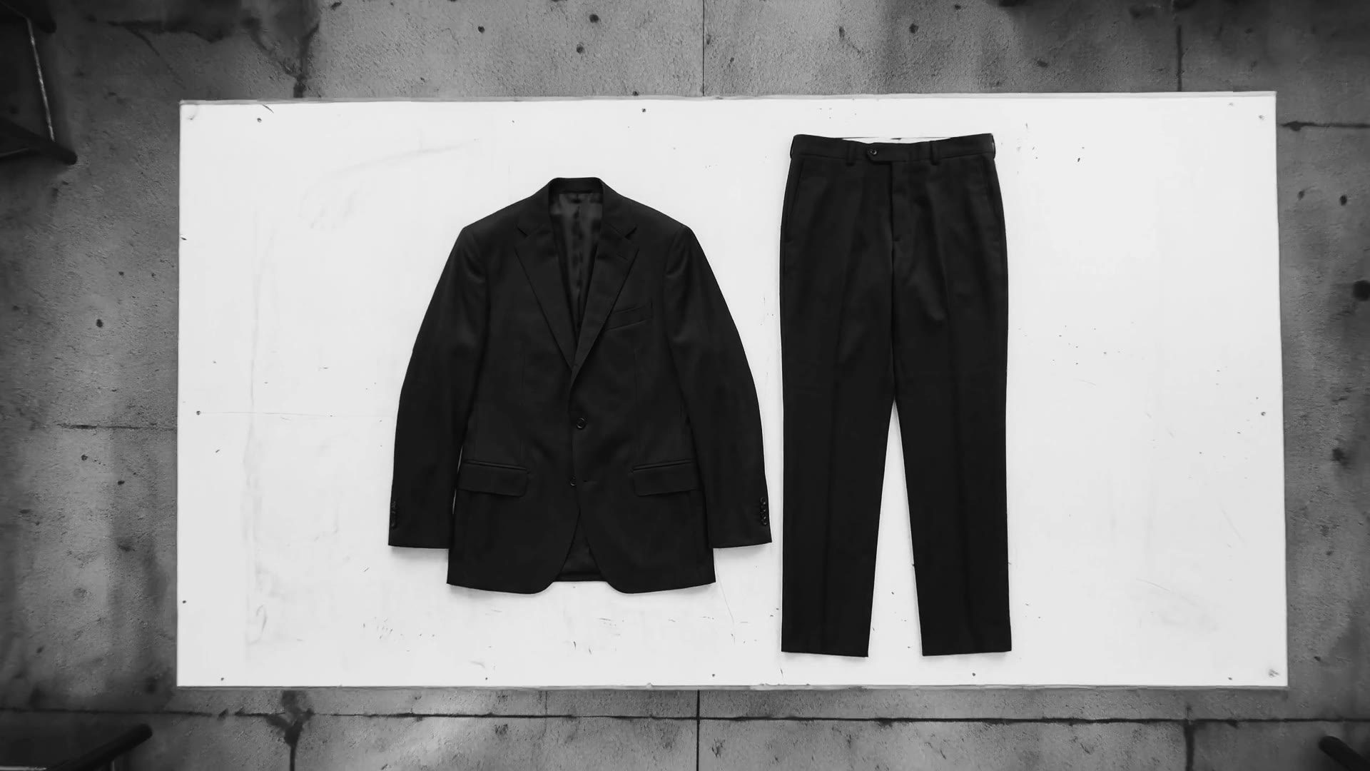 Seen from above: a finished dark suit, jacket and trousers, laid flat on a white cutting table.